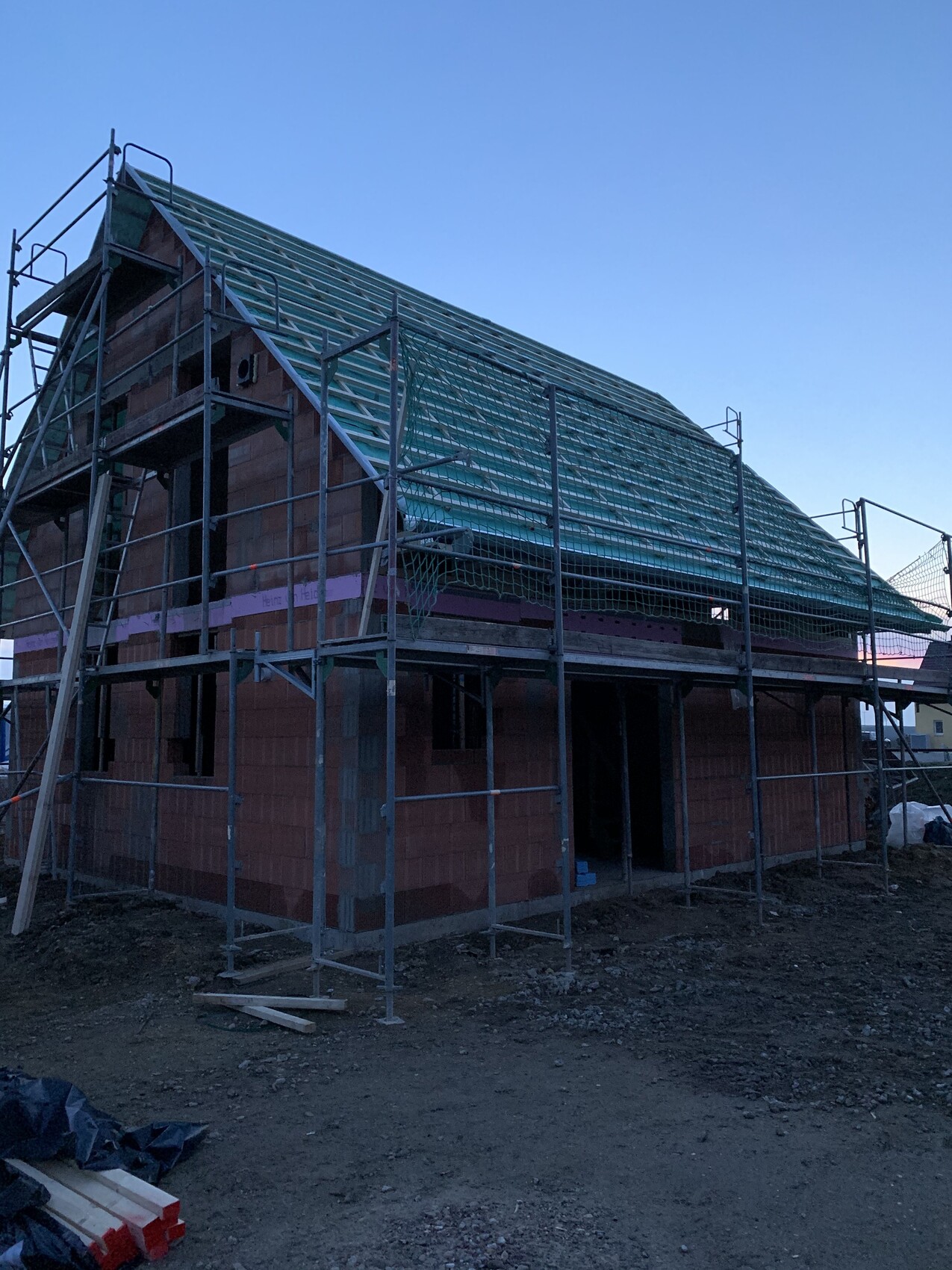 Rohbau eines Einfamilienhauses mit Gerüst und grünem Dachunterbau auf Baustelle.