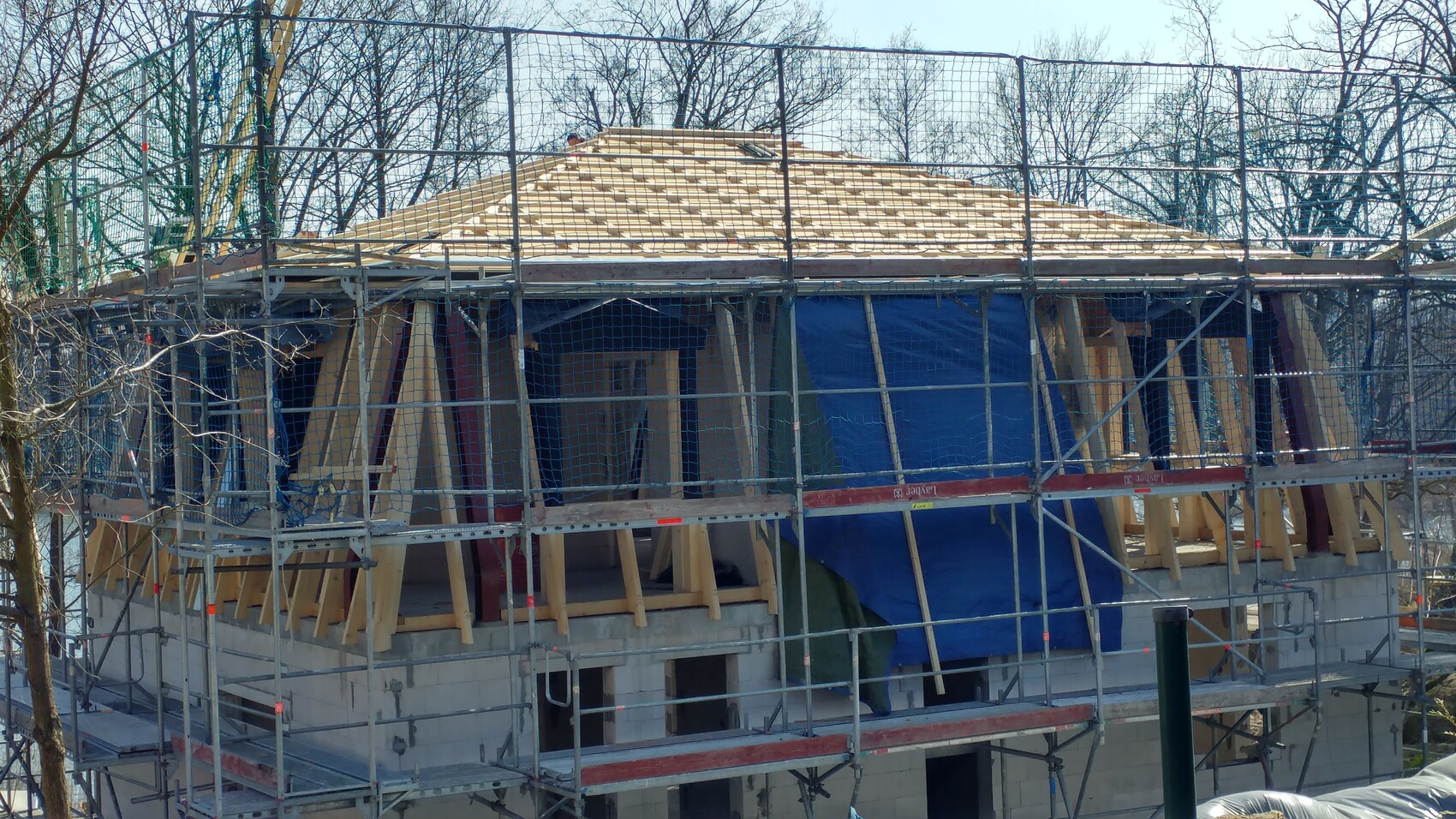Gebäude im Rohbau mit Gerüst, Holzbalken und blauen Planen um die Struktur.