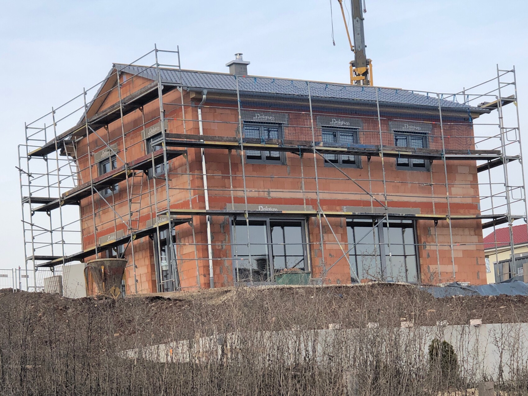 Ziegelhaus unter Bau mit Gerüst rundherum; Baukran im Hintergrund