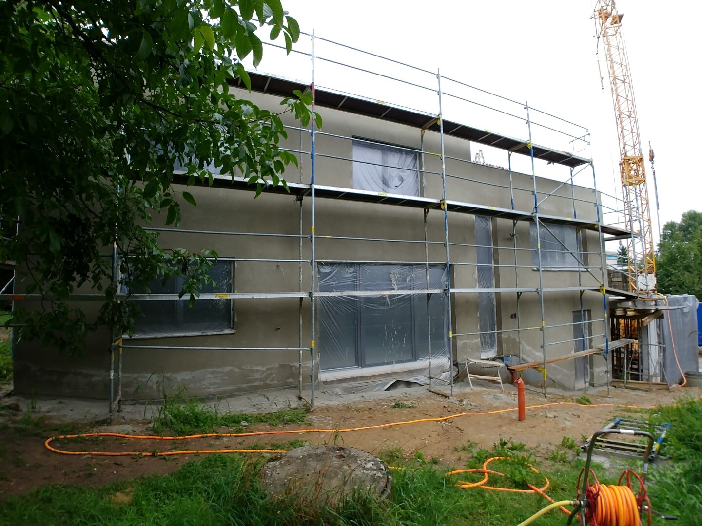 Außenansicht eines zweigeschossigen Hauses im Rohbau mit Gerüst und Baukran