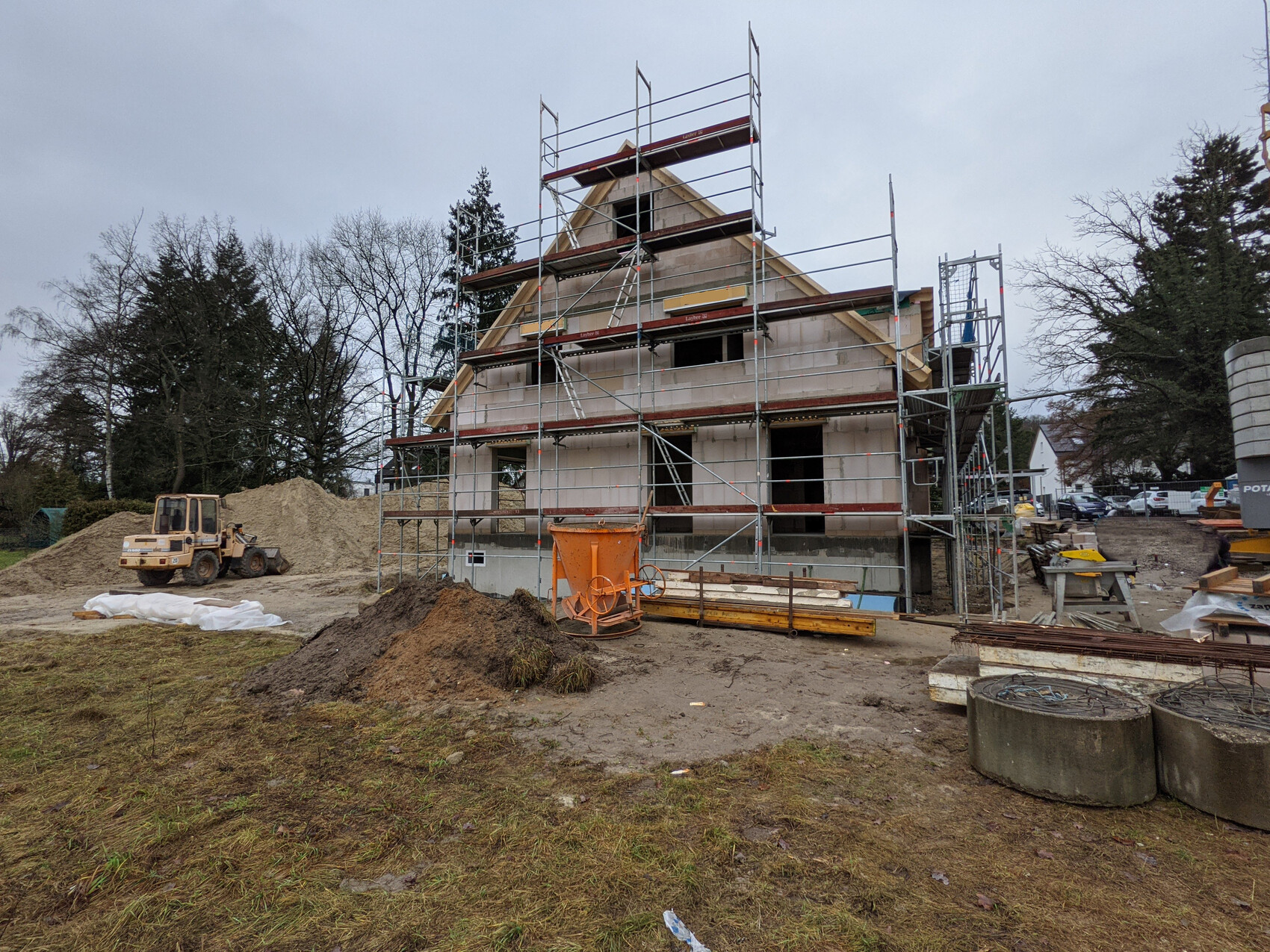 Neubau eines Hauses mit Gerüst, Baumaterialien, Sandhaufen und Baumaschinen