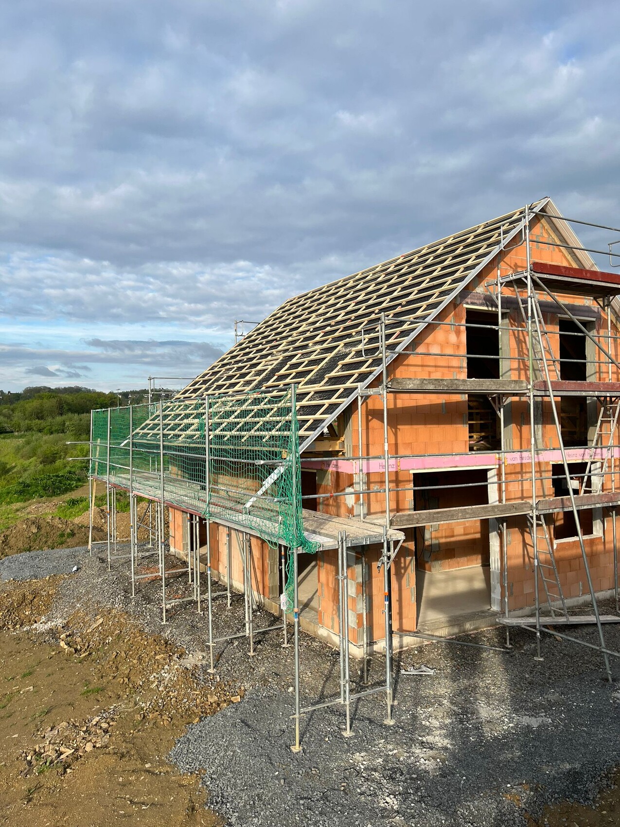 Rohbau eines Hauses mit Holz-Dachkonstruktion, Gerüst und Schutznetz.