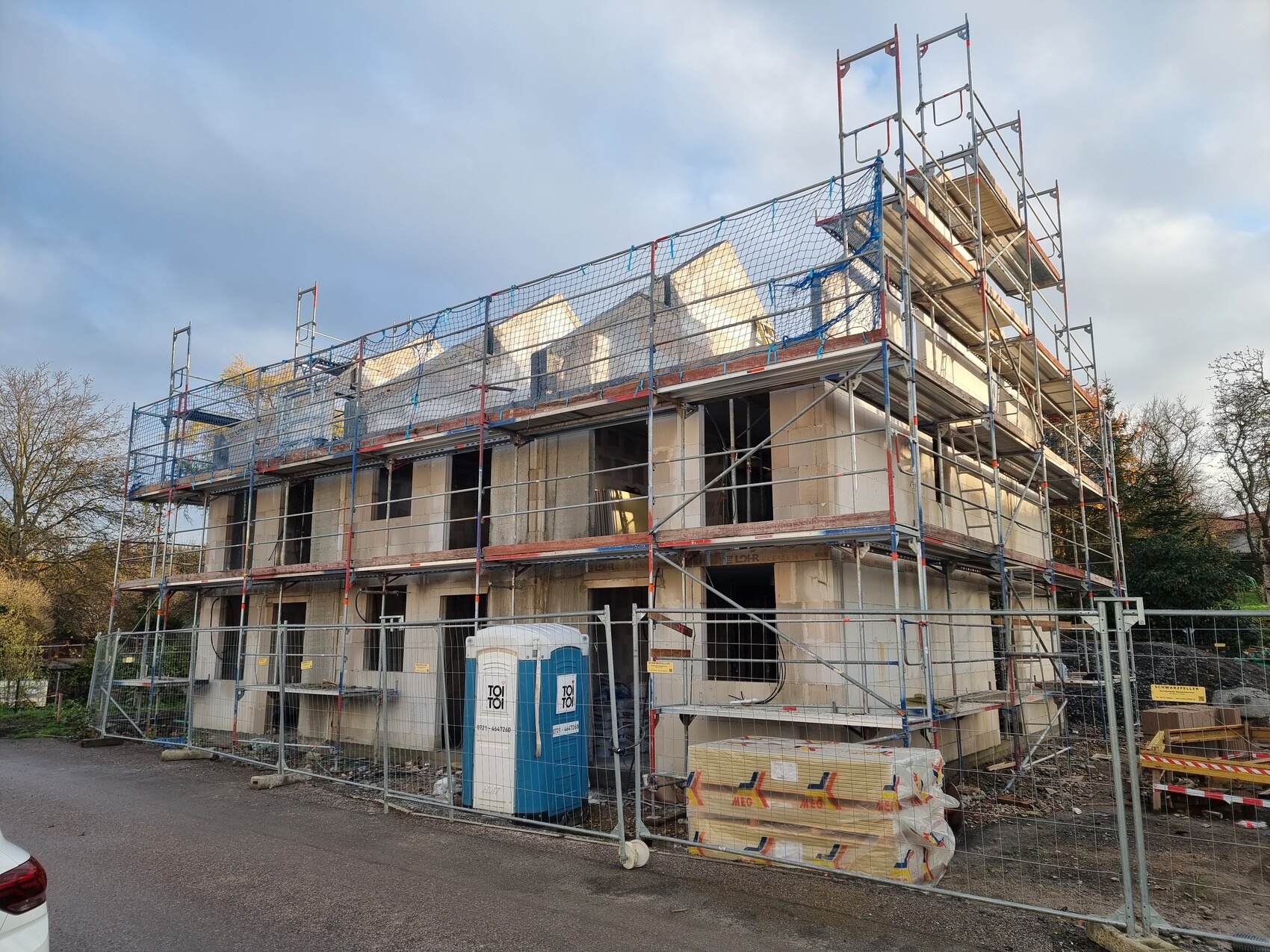 Neubauhaus mit Gerüst, unfertigen Außenwänden und Bauholz auf der Baustelle