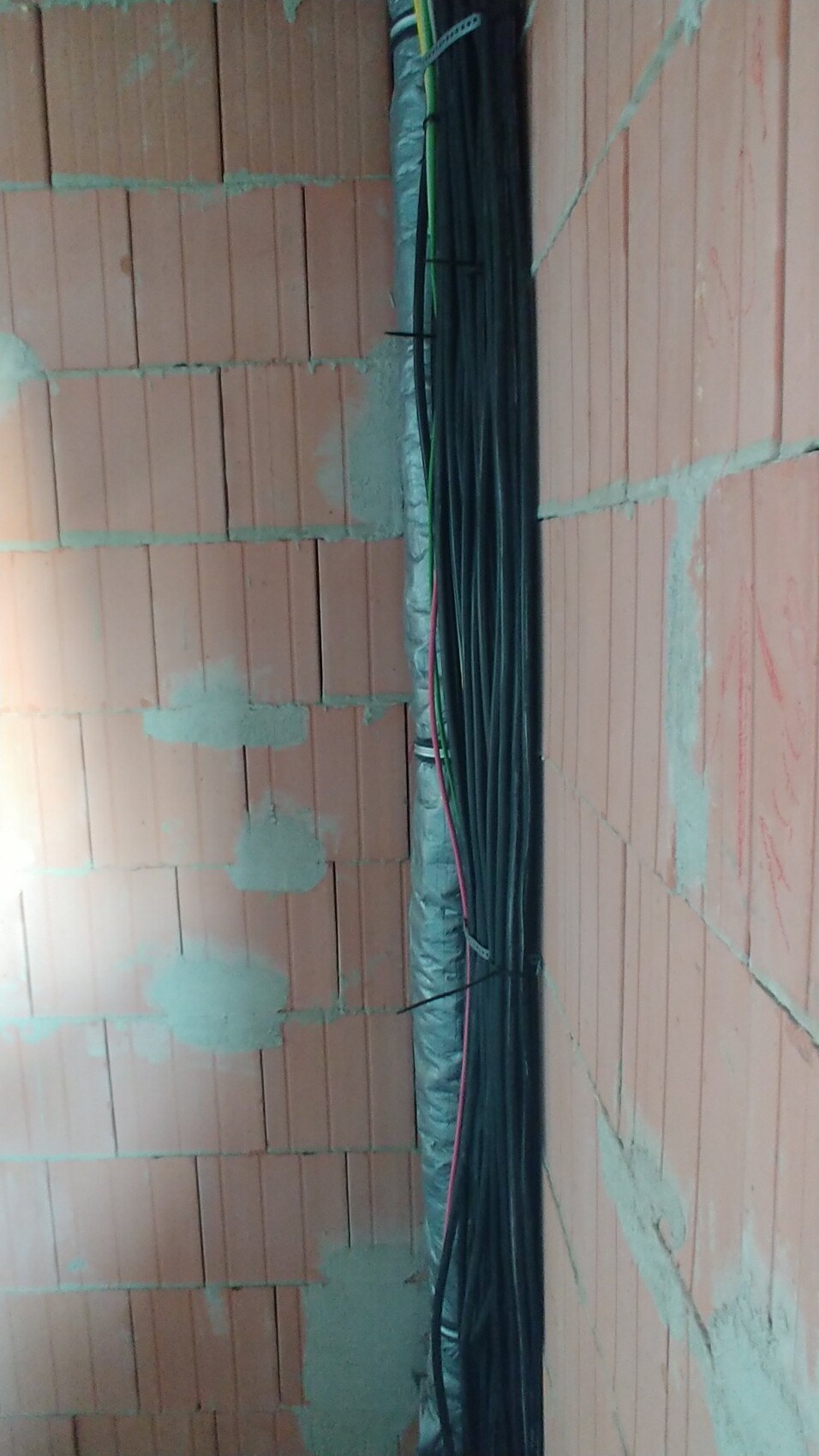 Rohbauwand aus roten Ziegeln mit Bündel schwarzer Kabel im Installationsbereich