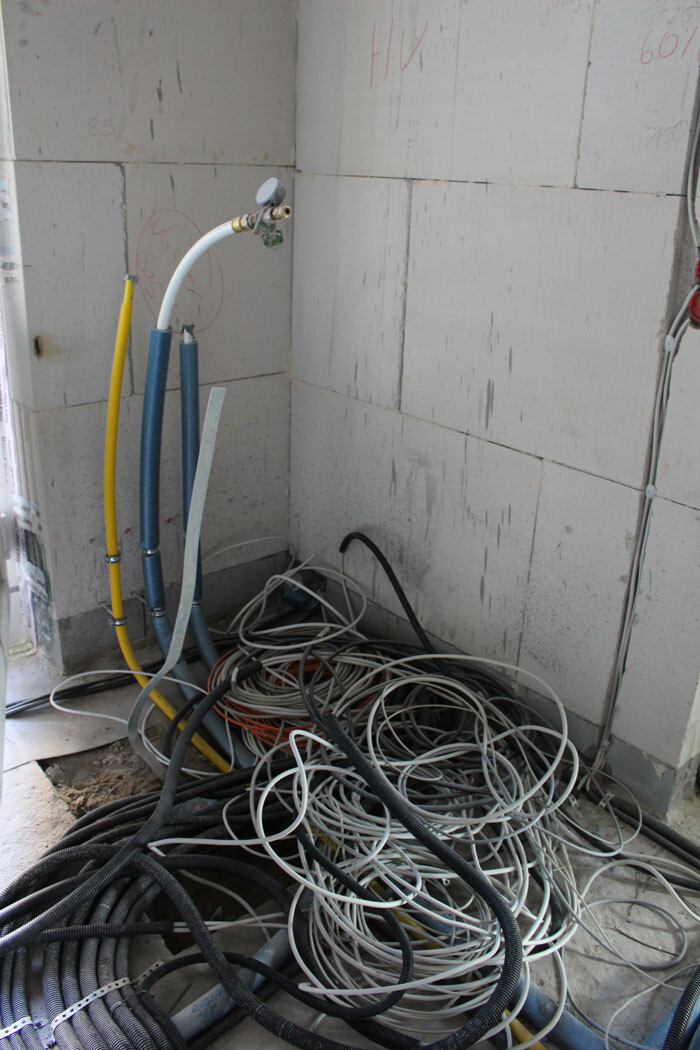 Baustelle: Kabelsalat und Schläuche liegen auf dem Boden neben einer Wand mit Dämmplatten.