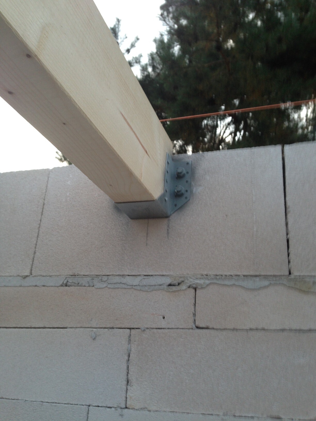 Holzbalken mit Metallwinkel befestigt an einer Betonfundamentwand während Rohbauarbeiten