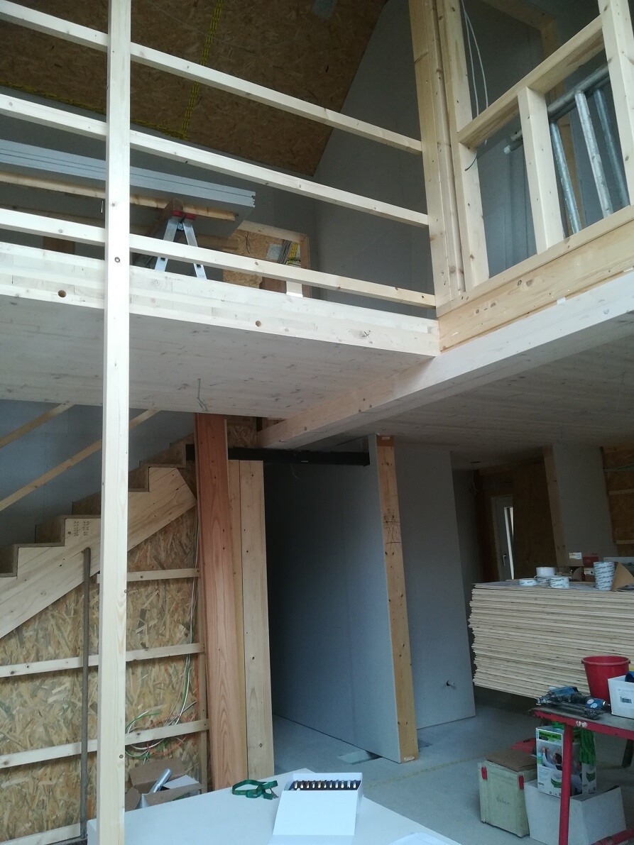 Innenbereich eines Neubaus: Holzkonstruktion, Treppe, Mezzanin-Geländer, Baustellenmaterialien.