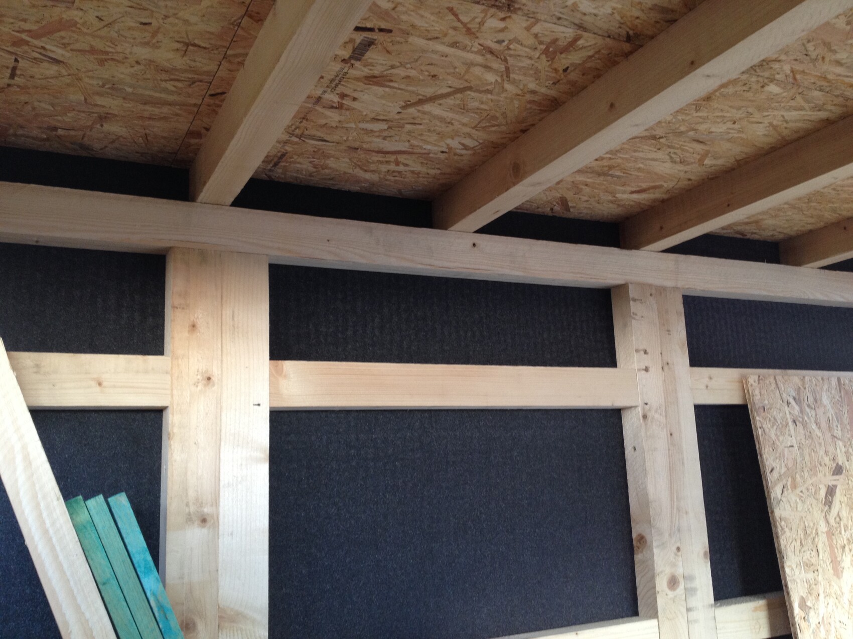Innenansicht eines Holzständerwerks mit OSB-Decke und schwarzer Dämmplatte.