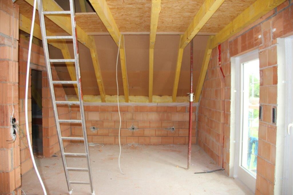 Innenraum einer Baustelle mit Ziegelwänden, Holzbalken und Leiter.