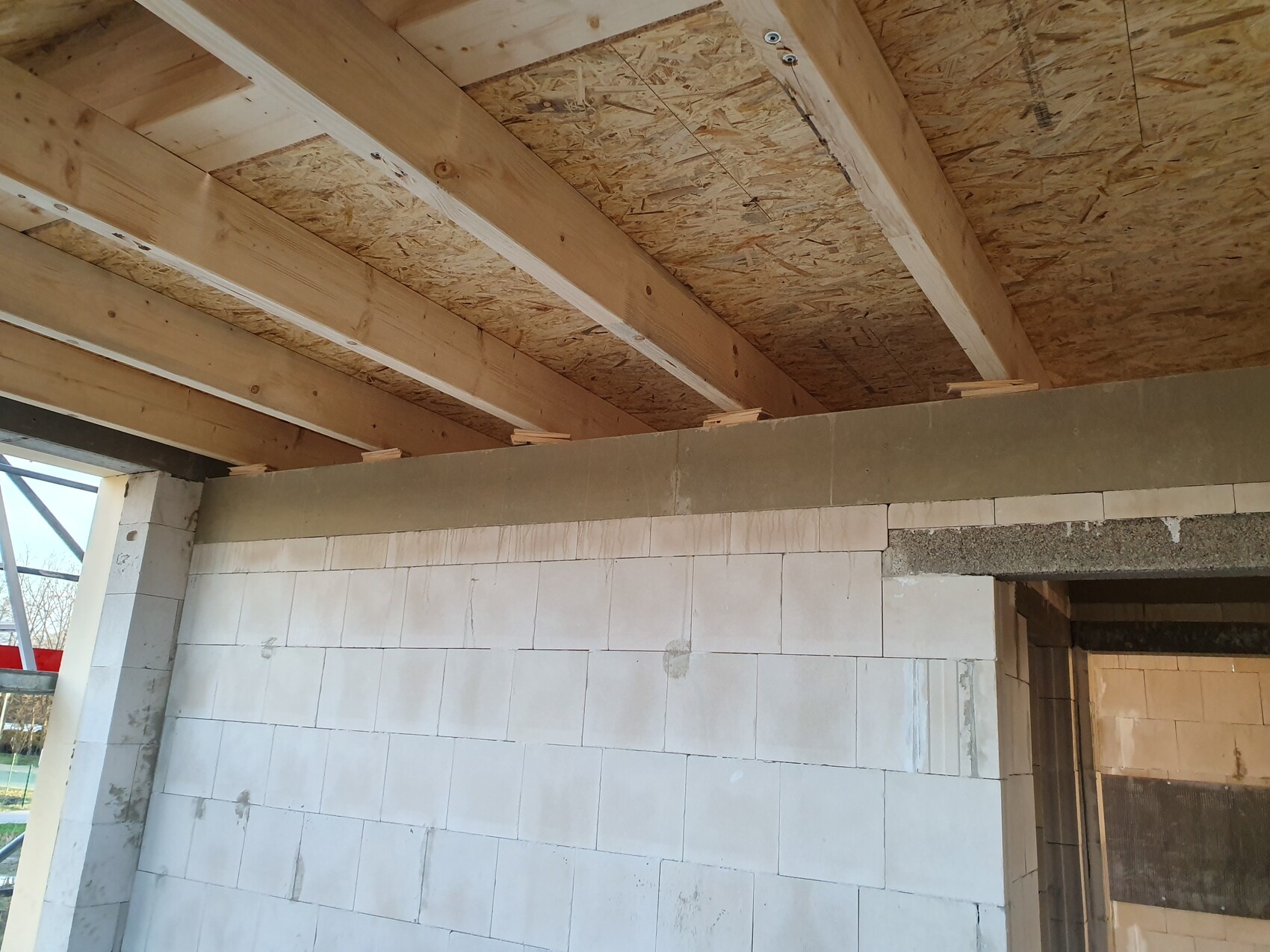 Innenansicht eines Rohbaus: Holzbalkendecke, OSB-Platten, weiße Betonblockwand.