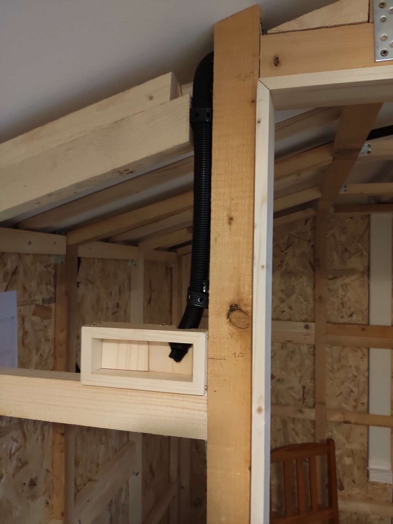 Innenbau mit Holzständerwerk, schwarzem flexiblen Kabelkanal und kleinem rechteckigen Holzkasten.