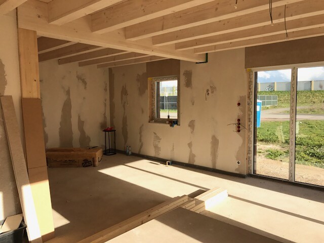 Unverputzter Innenraum im Rohbau mit Holzbalkendecke, unfertige Wände und Terrassentür.