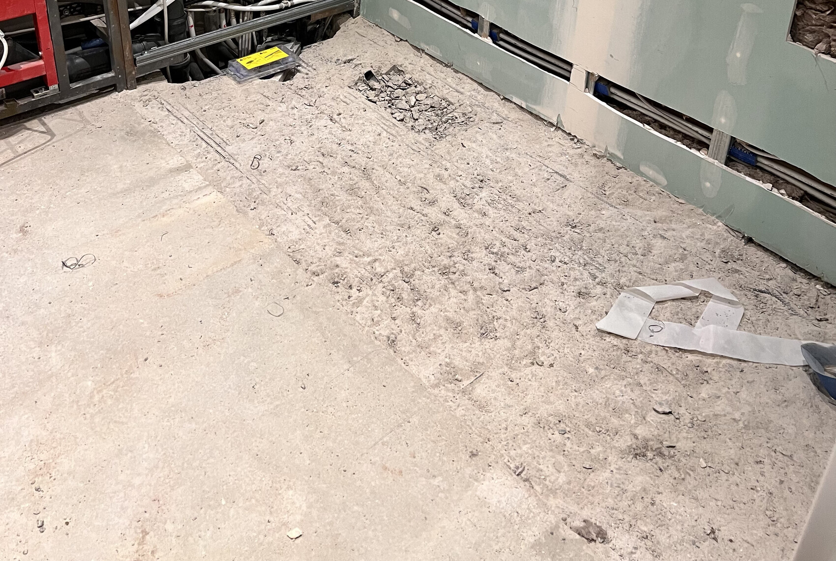 Innenbaustelle mit Bauschutt, rohem Boden, grüner Trockenbauwand und Bauwerkzeugen.