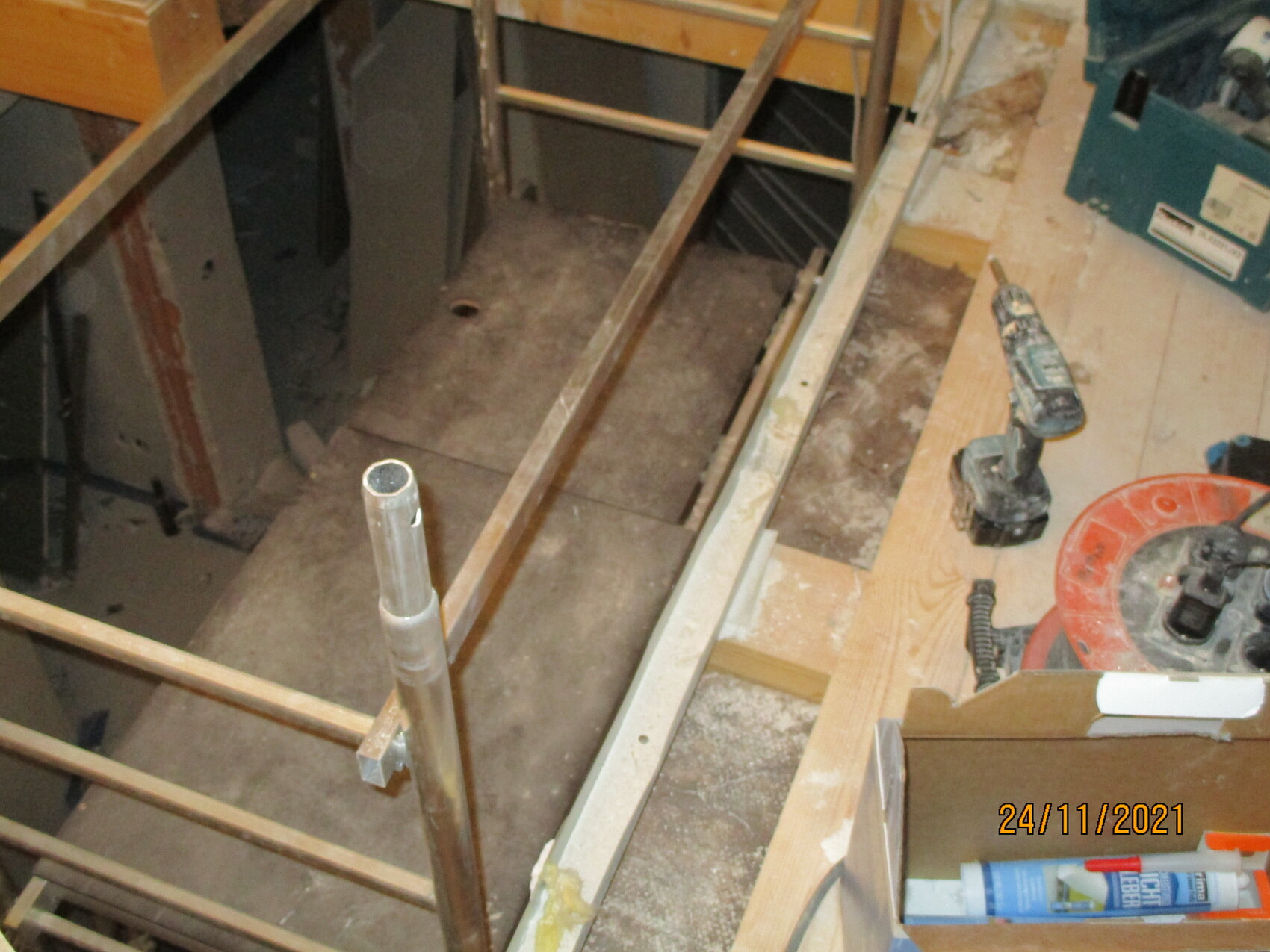 Innenraum einer Baustelle mit Holzrahmen, Rohr und Werkzeugen auf Staubboden.