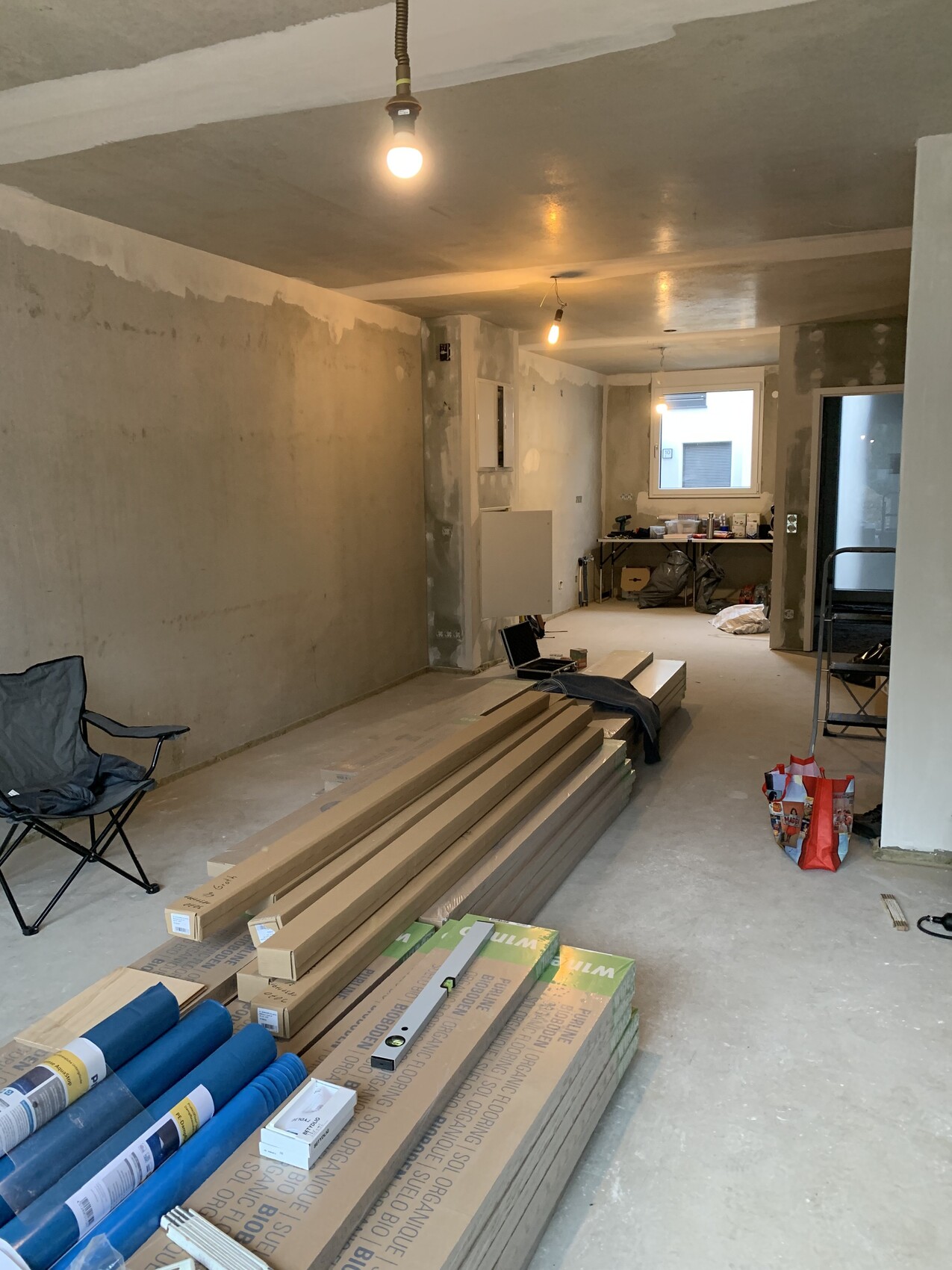 Unfertiger Innenraum einer Baustelle: Holzlatten, Platten, Werkzeug und Beleuchtung.