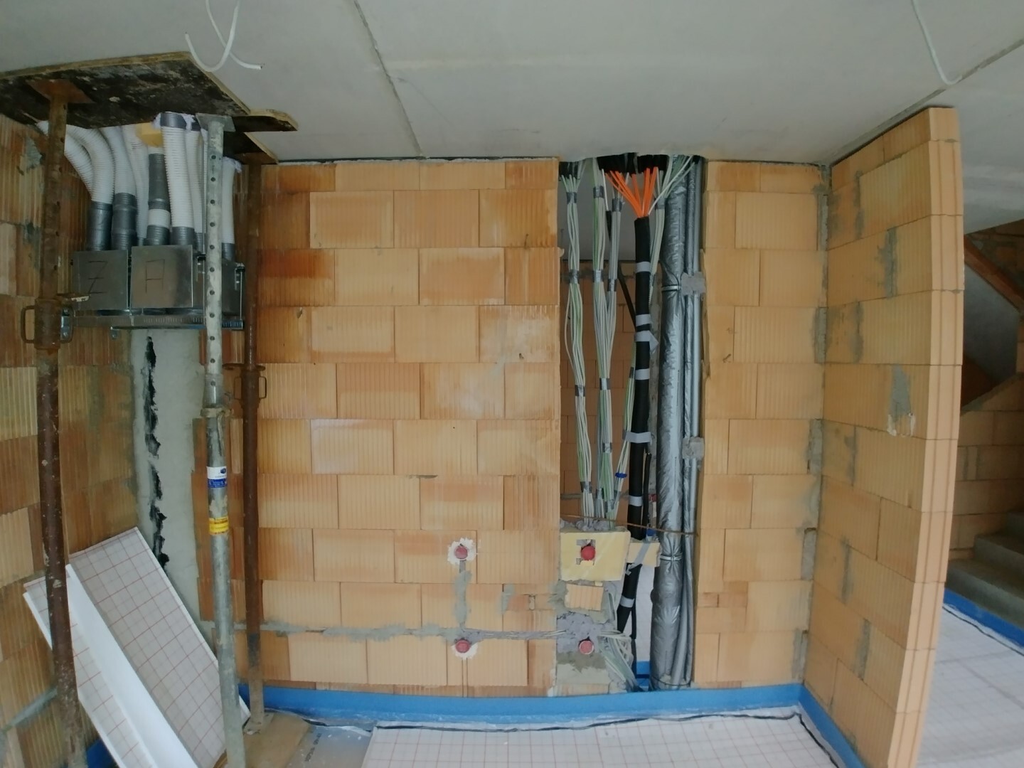Innenraum einer Baustelle mit Backsteinwänden, Kabelbündeln, Rohren und Installationen.