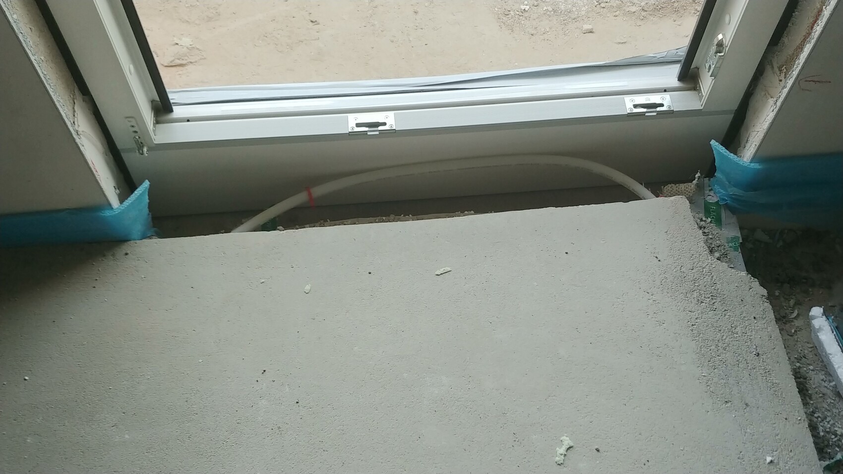 Rohbau Innenbereich mit Fensterrahmen, rohem Betonboden und blauer Baufolie am Rand