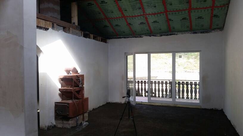 Unfertiger Innenraum mit Kamera auf Dreibein-Stativ, Holzregal und Glas-Tür zum Balkon