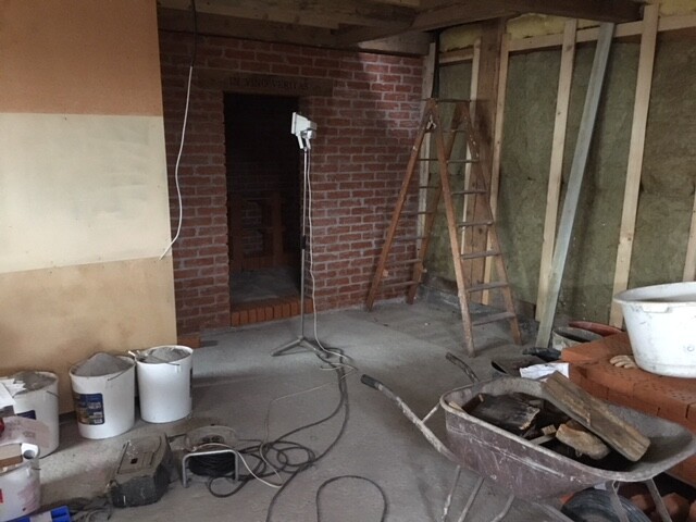 Innenraum einer Baustelle mit Backsteinwand, Leiter, Kabeln und Baumaterialien.