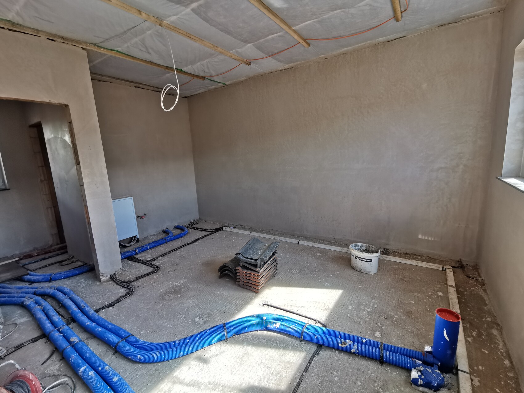 Unfertiger Innenraum einer Baustelle mit offener Decke, blaue Rohre auf dem Boden.