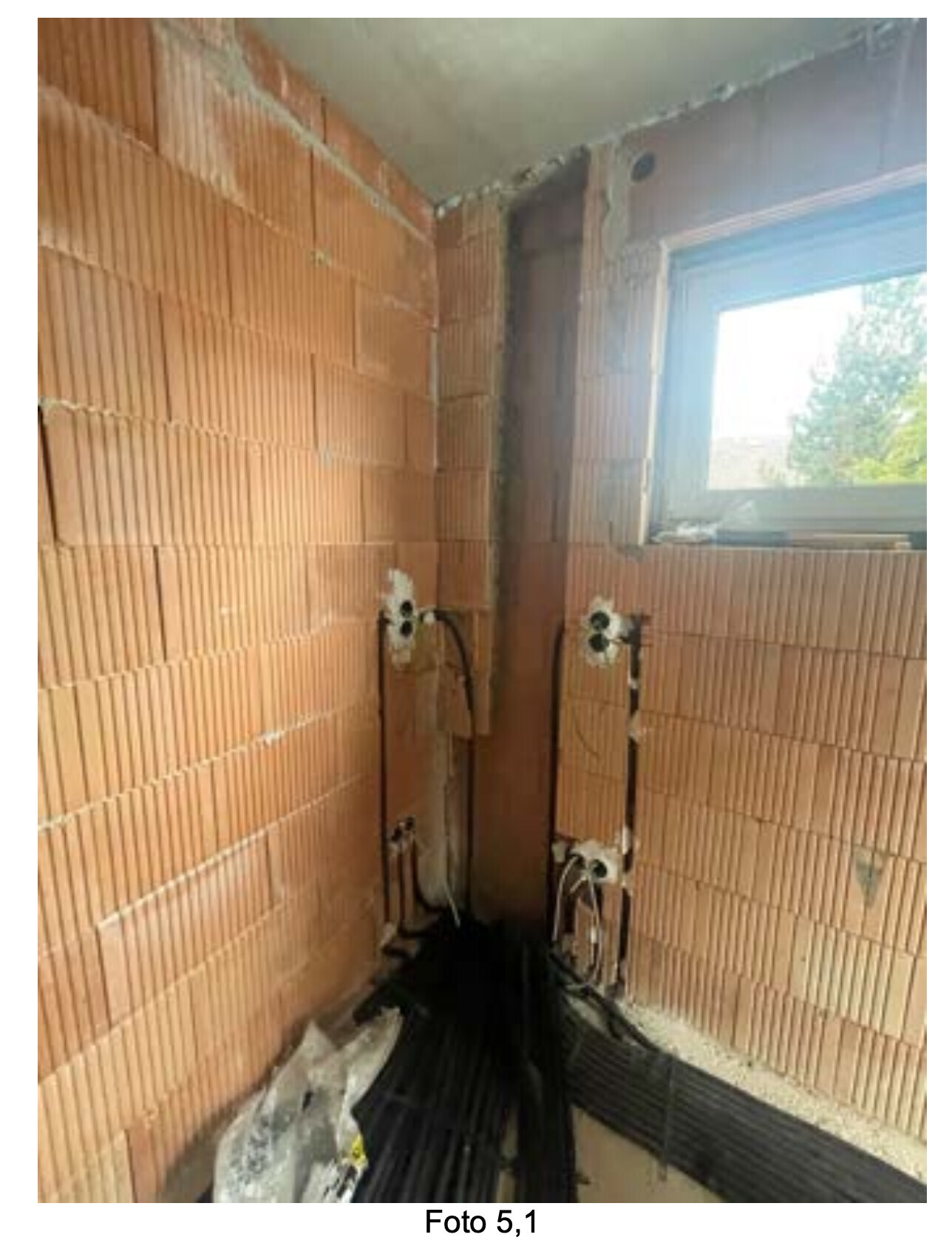 Rohbauzimmer mit roten Ziegelwänden, Kabeln am Boden und Fensteröffnung.