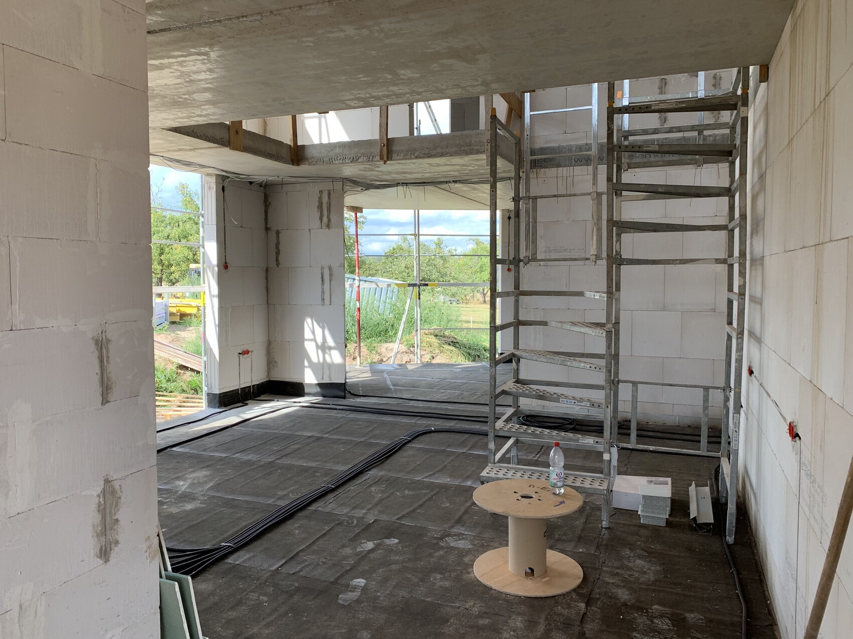 Unfertiger Innenraum einer Baustelle: Gerüst, Kabel, weiße Blöcke und Blick nach draußen.