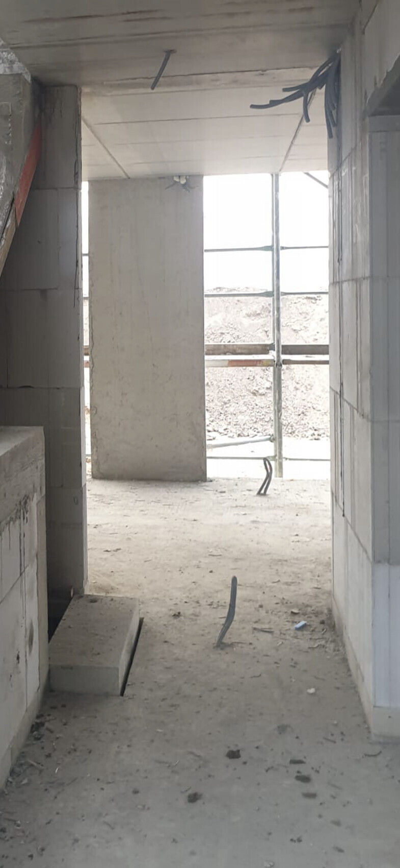 Unfertiger Betonbau-Innenraum: Blick durch Flur mit Stützen, Kabeln, Staub.