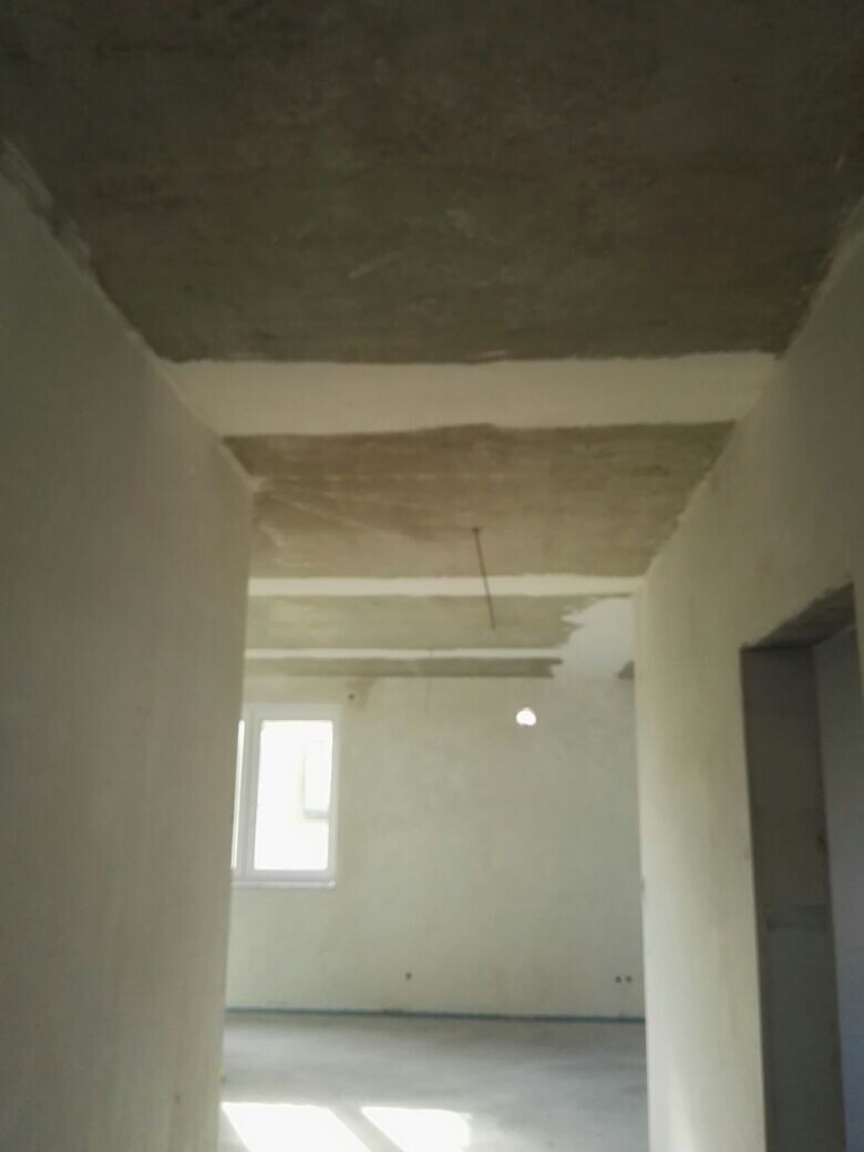 Unfertiger Innenraum eines Rohbaus mit Beton-Decke, unverputzten Wänden und Fenster.