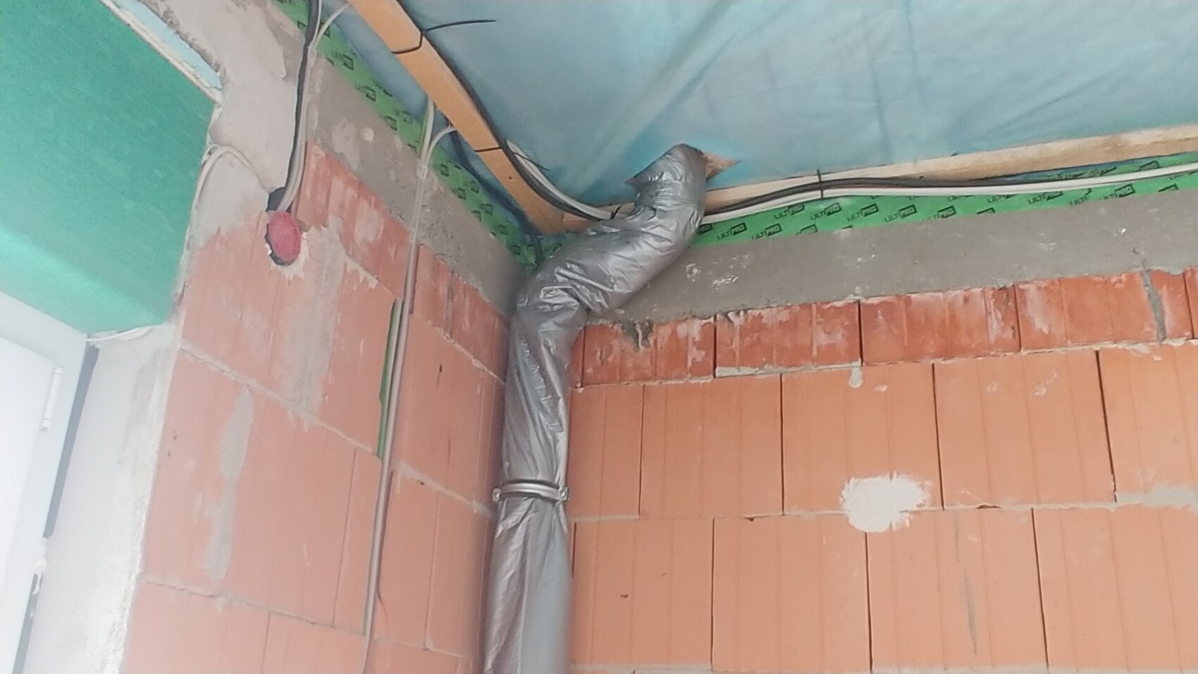 Rohbau-Innenraum mit Ziegelwand, flexiblen Rohren und Dämmung an Decke