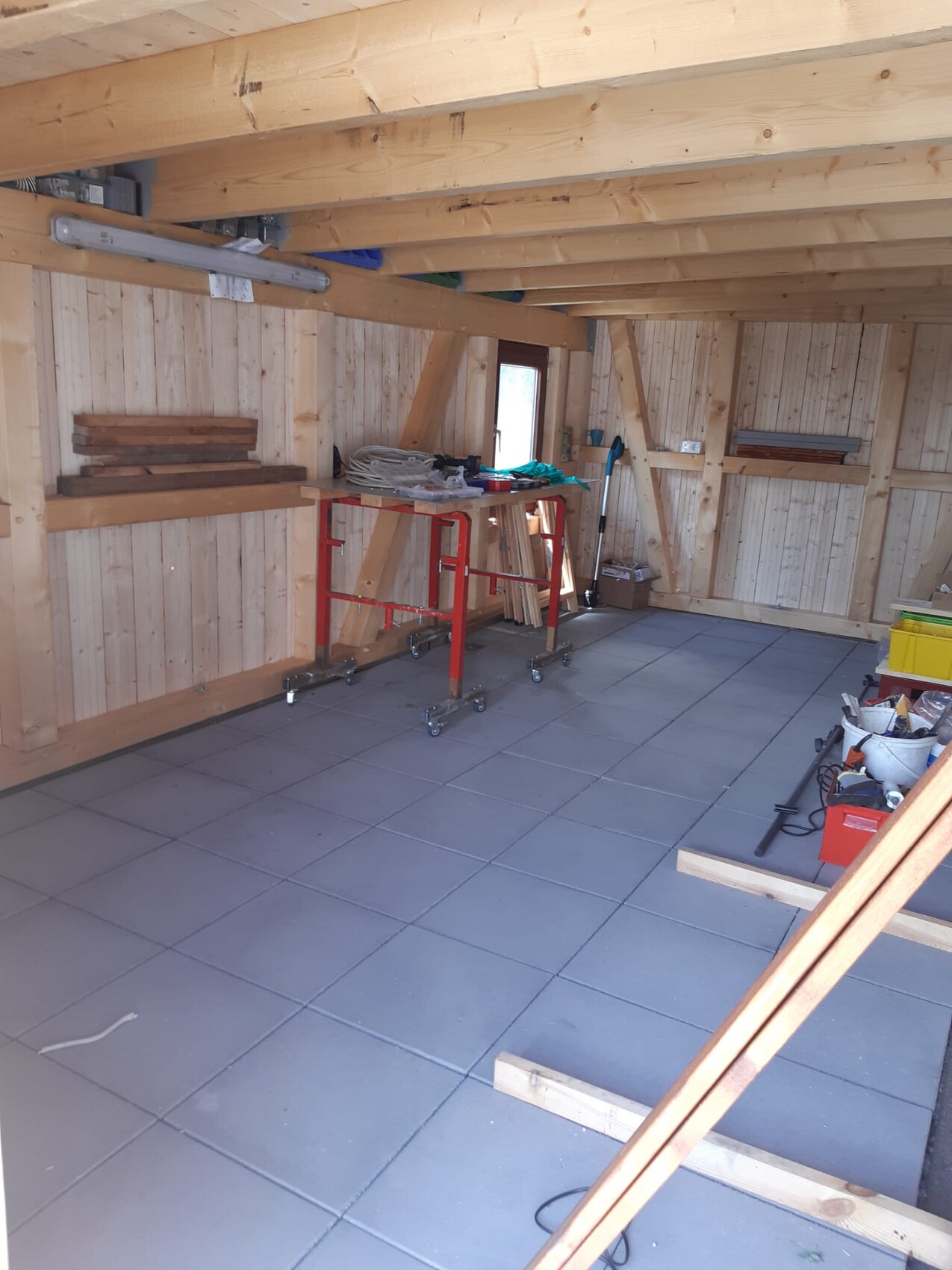 Rohbau-Innenraum eines Holzhauses mit Bauwerkzeugen, Werkbank und Baumaterialien.