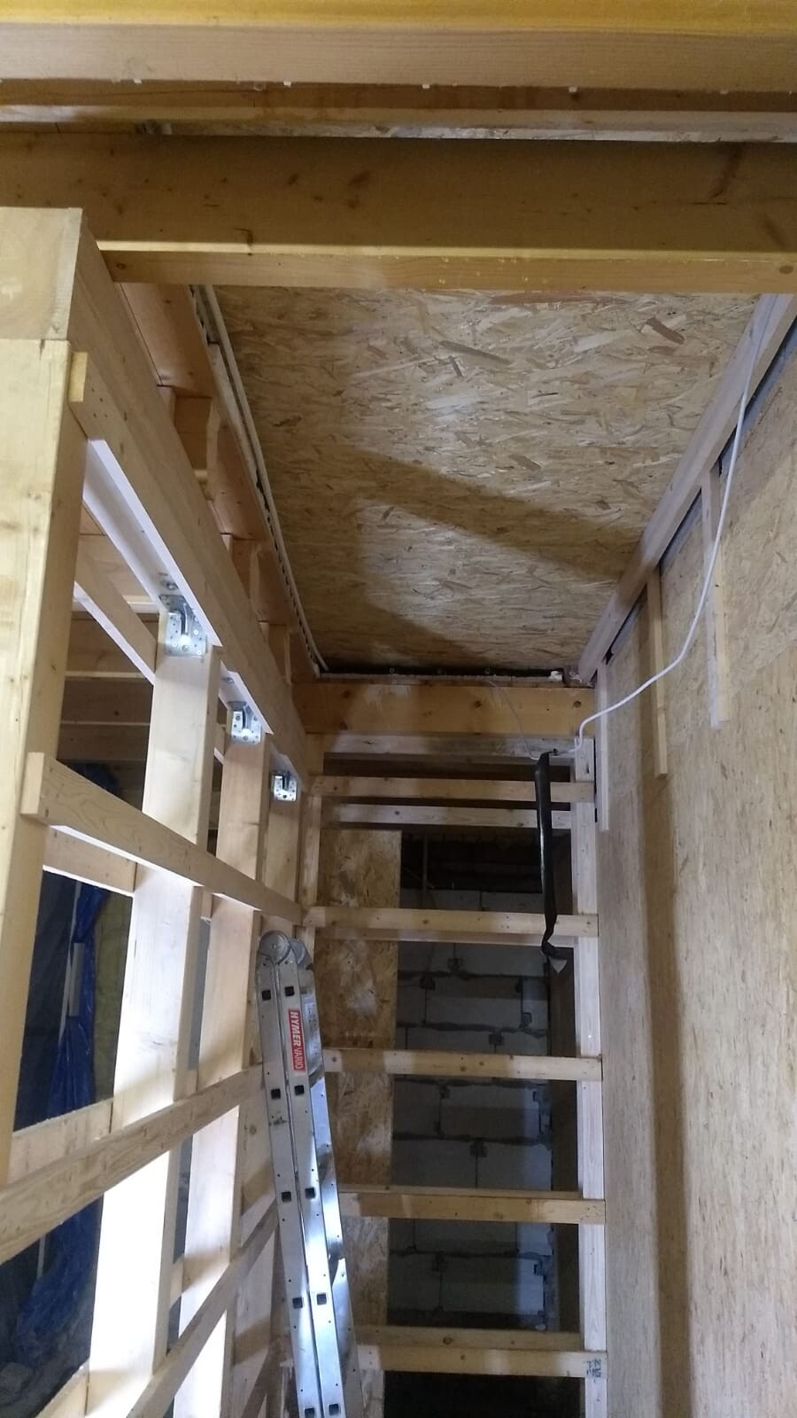 Rohbau-Sicht: Holzständerwerk, OSB-Decke, Leiter und sichtbare Elektroinstallation.