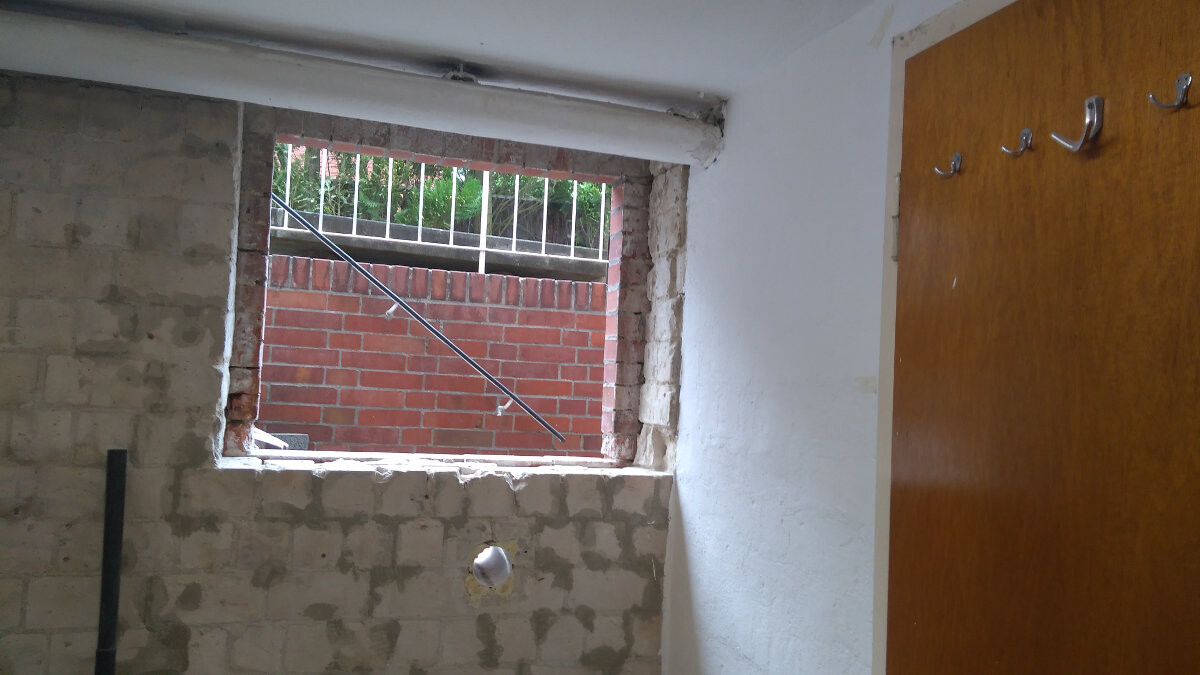 Rohbauzimmer mit offener Fensteröffnung in unverputzter Ziegelwand; rechte Holztür.