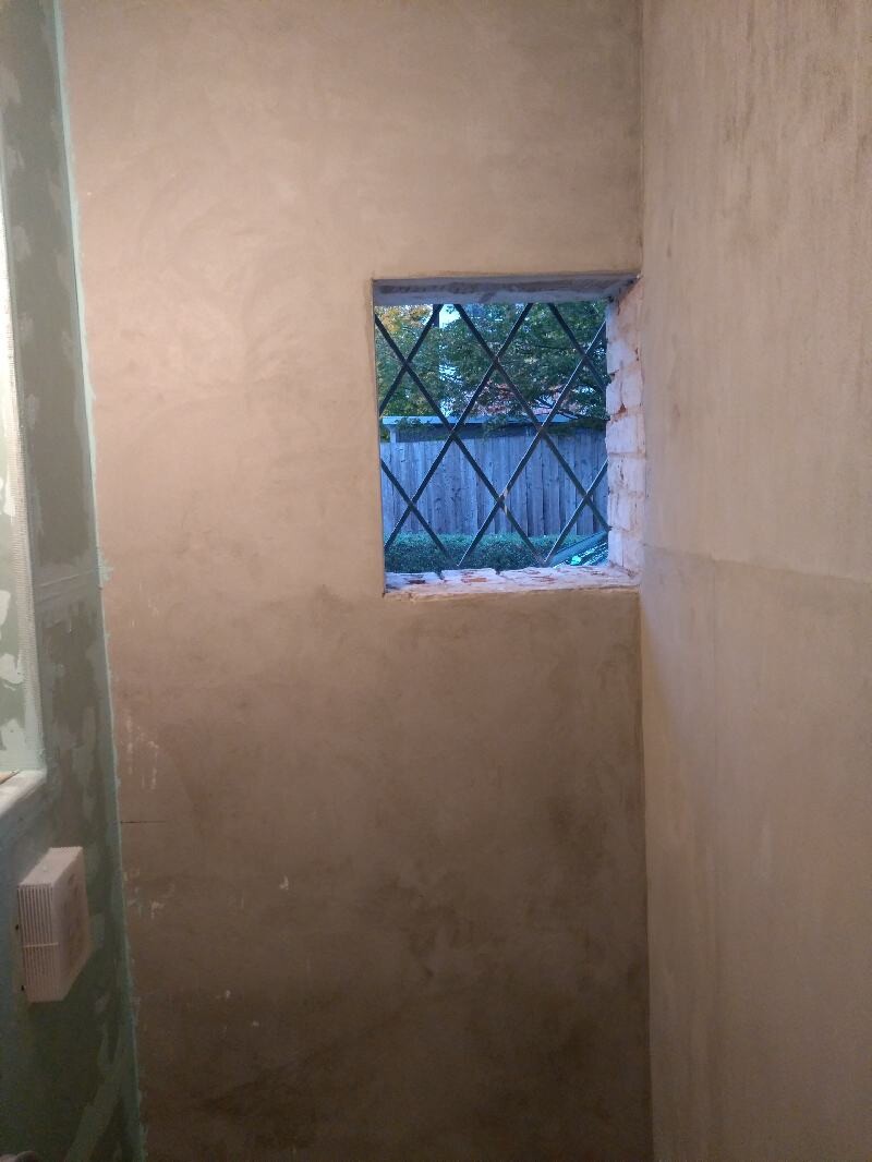 Innenraum einer Baustelle: kleines quadratisches Fenster mit Gitter, Blick nach Garten.