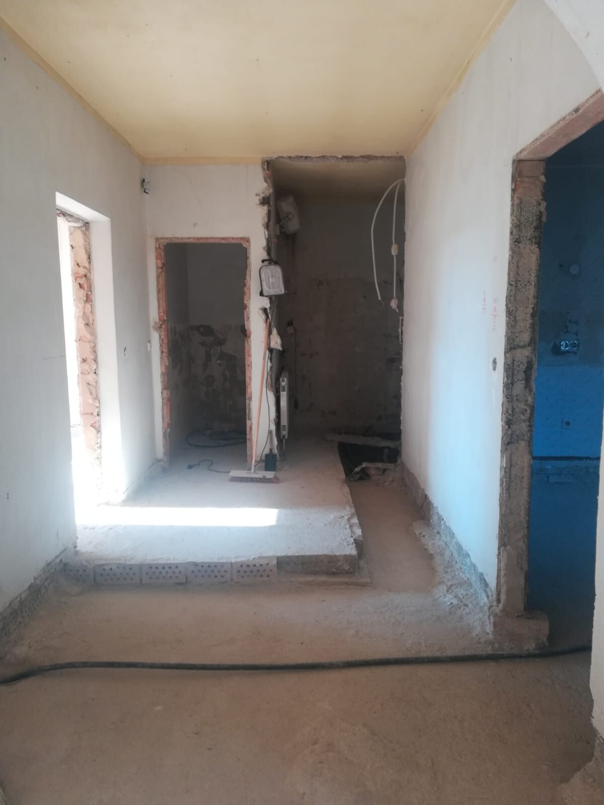 Rohbau-Flur mit offenen Wänden, losen Kabeln, Baugeräten und unebenem Betonboden