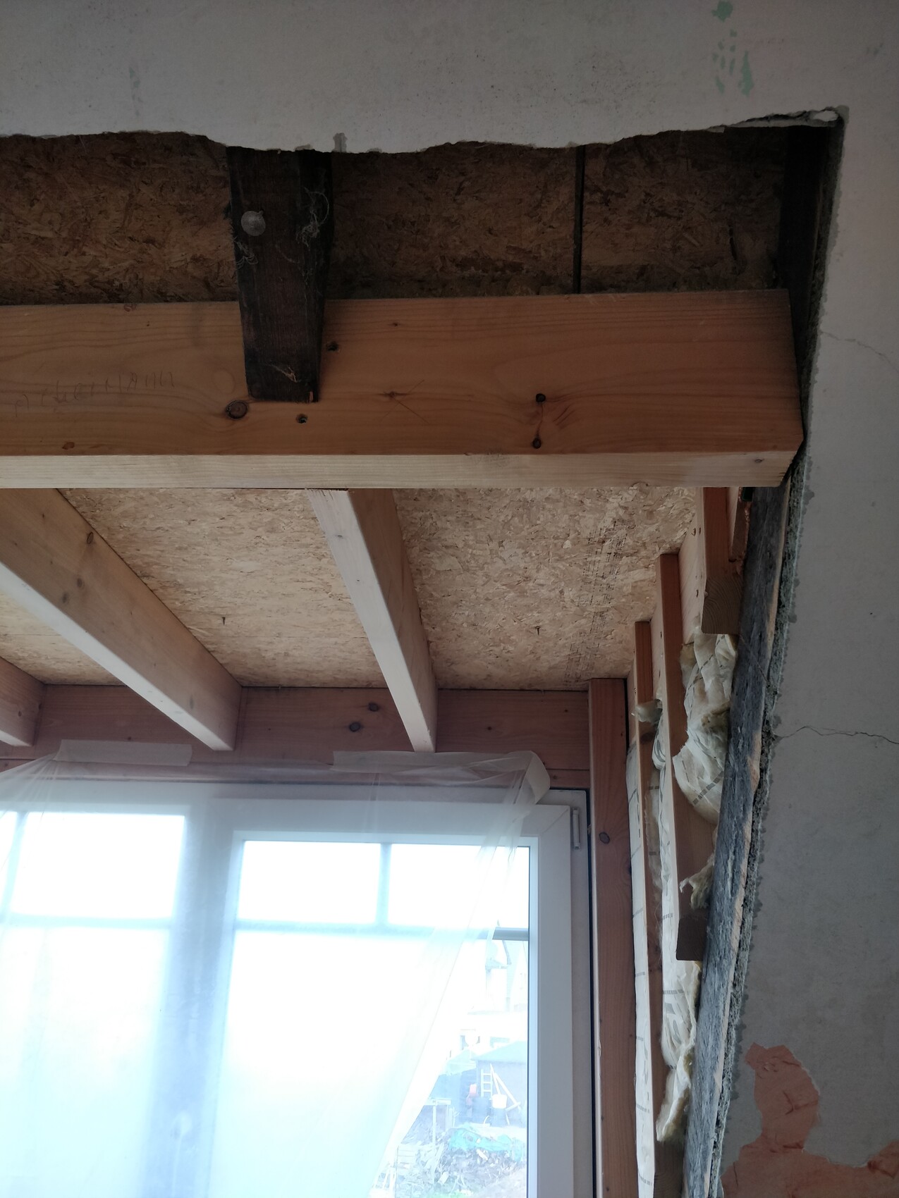 Innenraum einer Baustelle: freigelegte Decke mit Holzbalken, Fenster mit Folienabdeckung.
