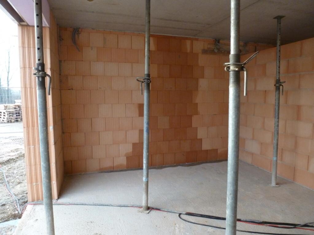 Innenraum eines Bauprojekts: rote Ziegelwände, Stahlstützen und Betonboden.