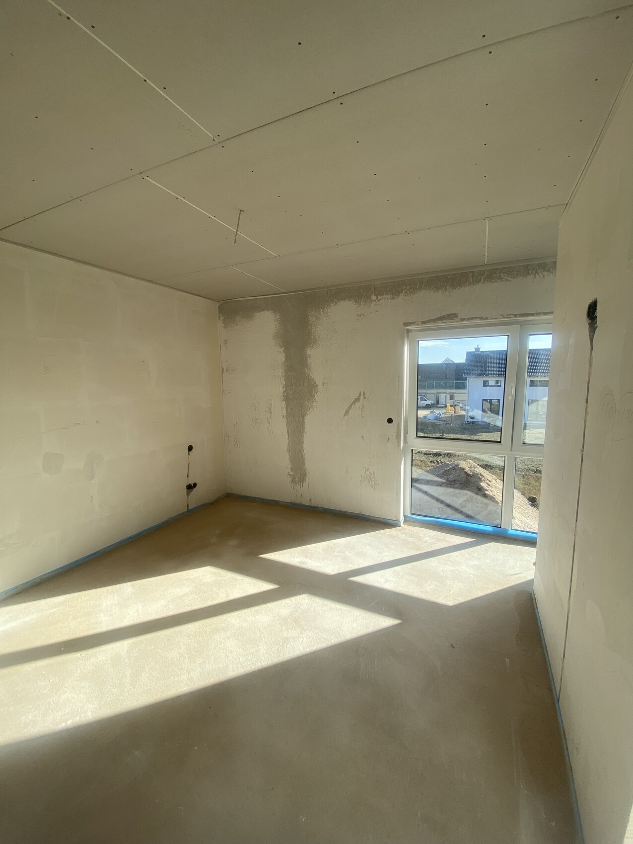 Rohbauzimmer mit unfertigen Wänden, Decke, Fenster mit Blick nach außen; Licht fällt herein.