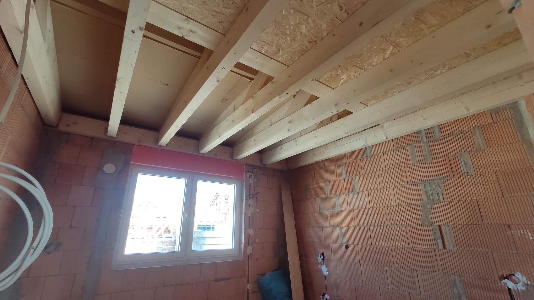 Unfertiger Innenraum: Sichtbare Holzbalkendecke, Ziegelwände und Fensterfront.