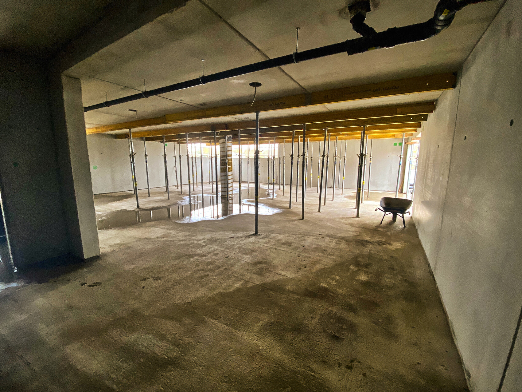 Große Bauhalle mit vielen Stützen, Pfützen auf dem Boden und einer Schubkarre.