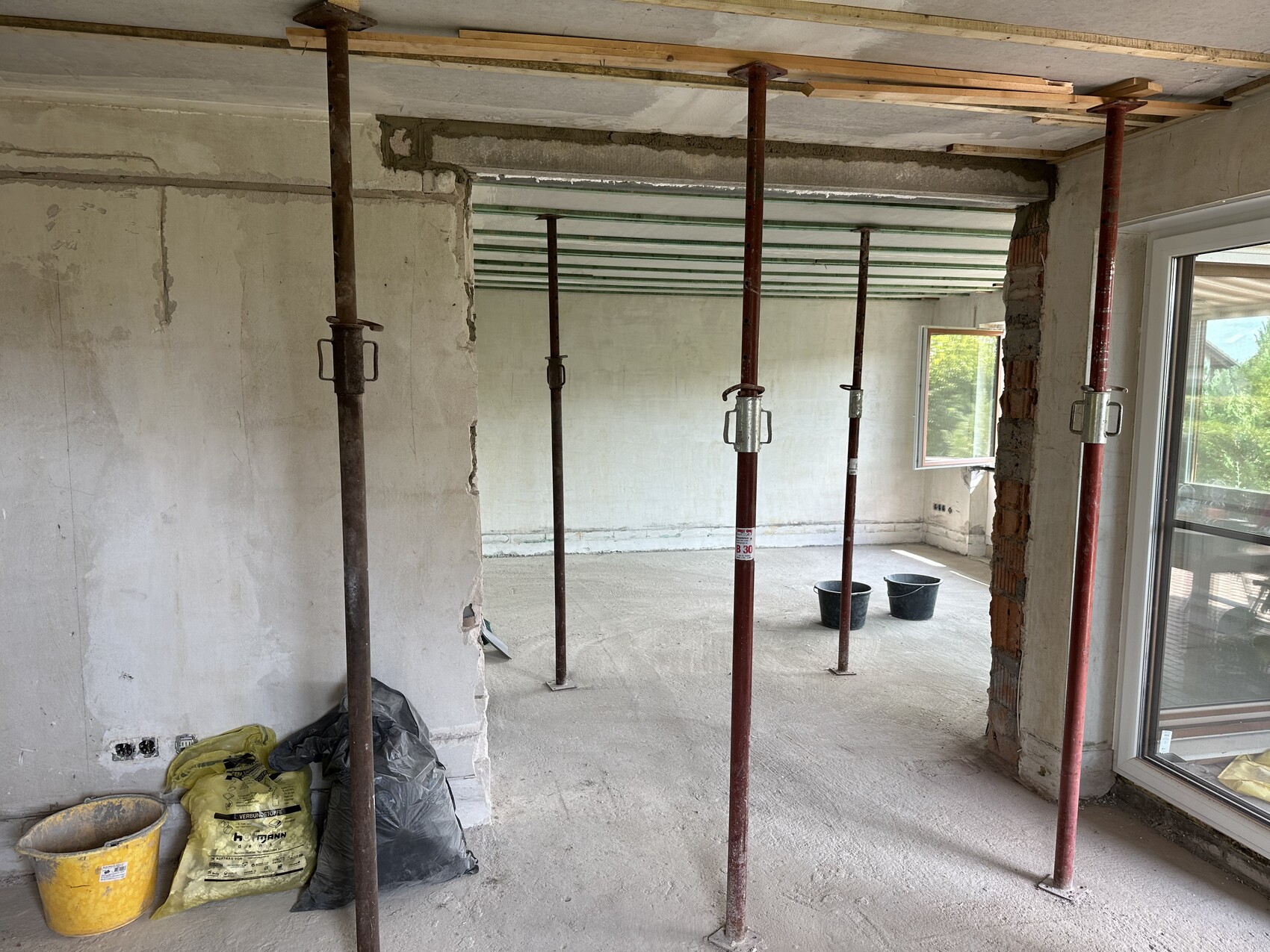 Innenraum im Rohbau mit roten Stahlstützen, Bauwerkzeugen und Fenstern.