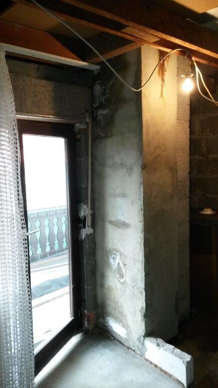 Unfertiger Rohbau-Innenraum mit Sichtbetonwand, freiliegende Kabel, Balkontür
