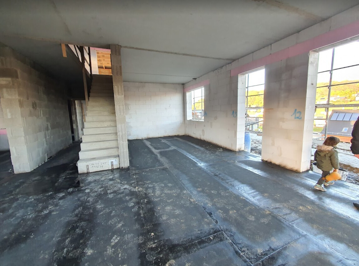 Unfertiger Innenraum eines Bauprojekts: Treppe links, Fenster rechts, ein Kind läuft.