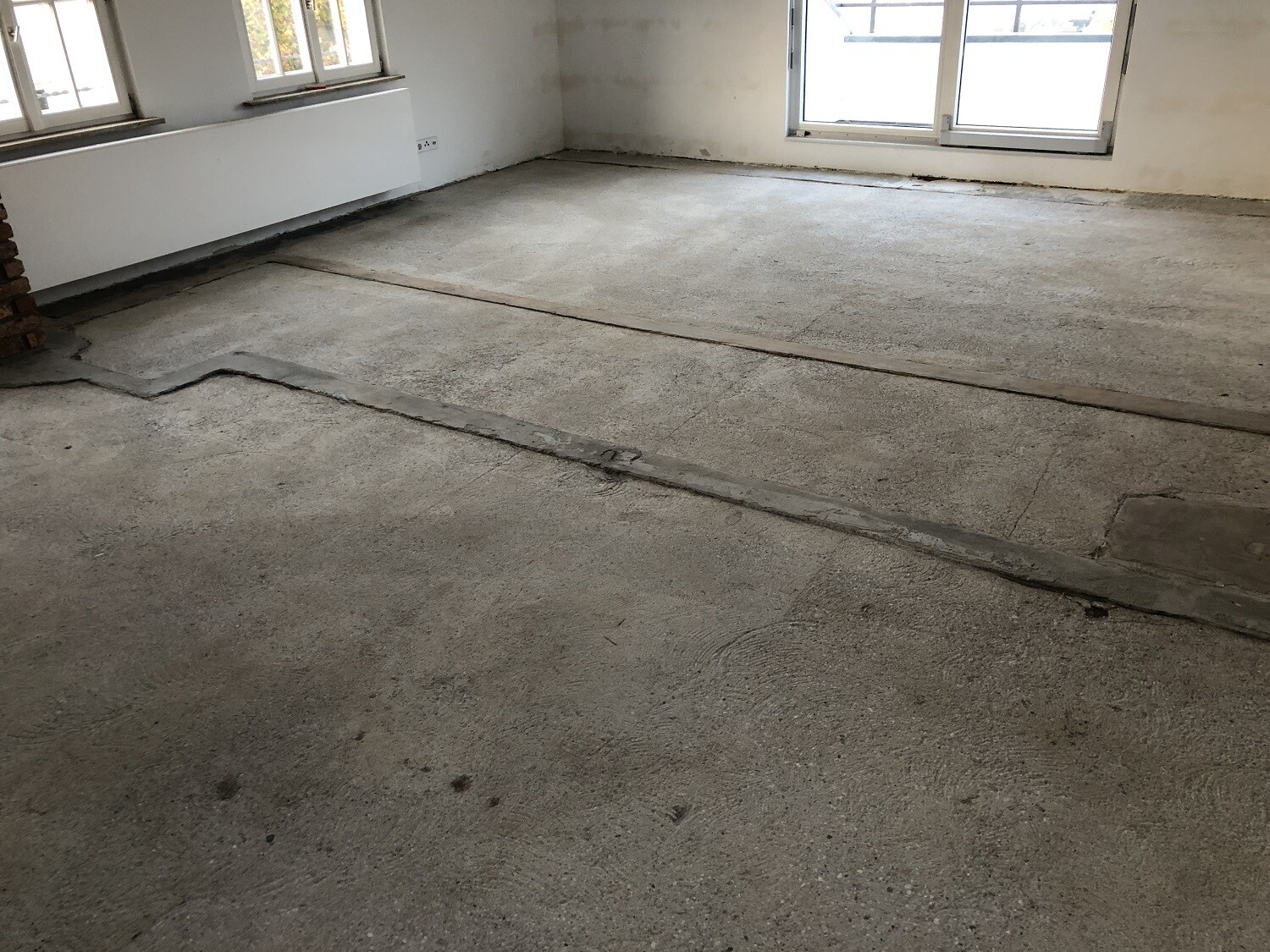 Leerer Innenraum im Rohbau mit rohem Betonboden, Fenstern und unvollständigen Wänden.