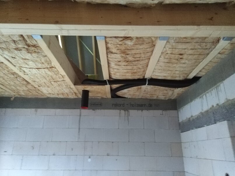 Unverputzter Keller mit Dämmung zwischen Holzbalken, schwarze Rohrleitung verlegt.