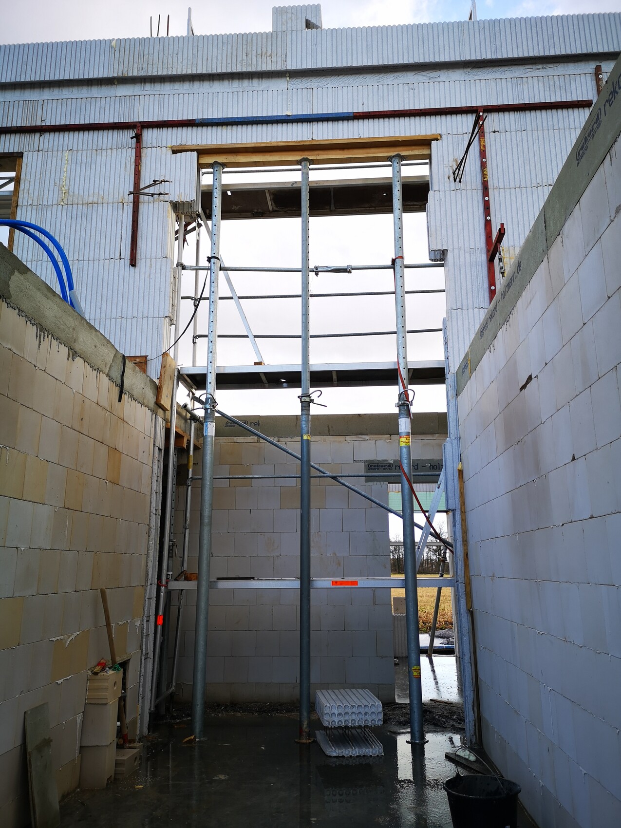 Innenraum einer Baustelle mit Gerüst, Betonwänden und Pfützen auf dem nassen Boden.