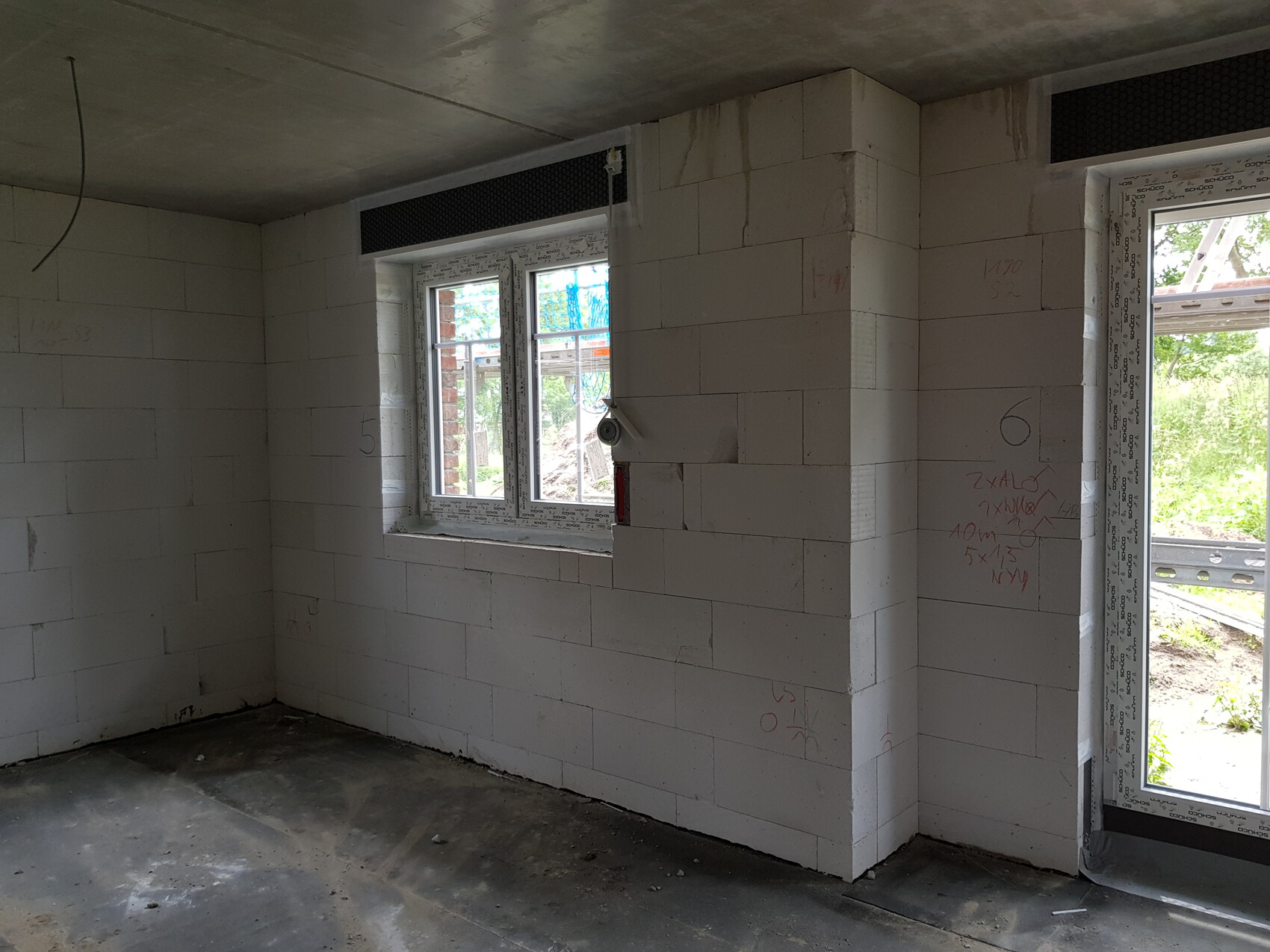 Unfertiger Innenraum mit weißen Blöcken, Fenster zur Außenansicht und Tür nach draußen.