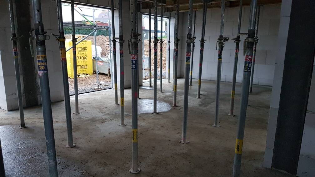 Innenraum einer Baustelle mit vielen Metallstützen (Acrow-Props) und feuchter Betonboden.