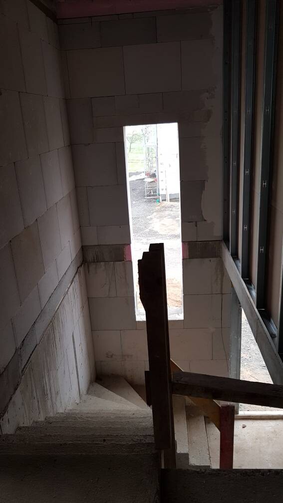 Rohbau-Treppenhaus: Betonwände, Geländer, Blick durch rechteckige Öffnung nach außen.