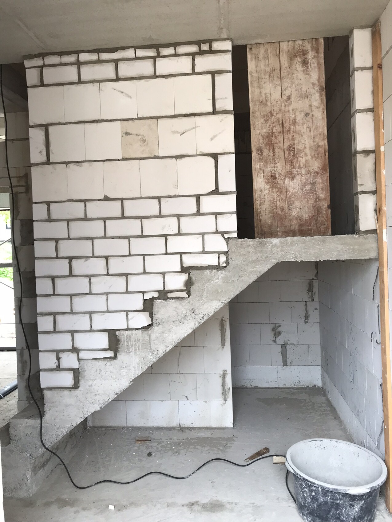 Rohbau-Innenbereich mit Betonstufen, weißer Ziegelwand und Bauwerkzeugen.
