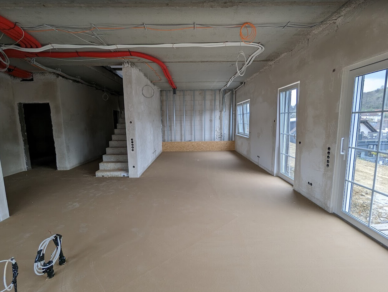 Rohbau-Innenraum mit Treppe, offenen Kabeln und unfertigen Wänden im Baufortschritt